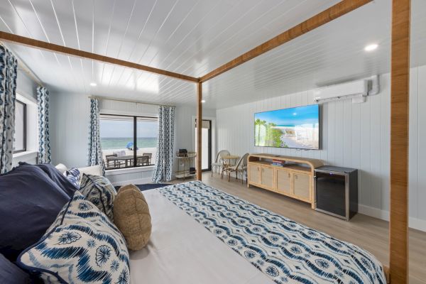 A modern bedroom with ocean views, featuring a large bed, flat-screen TV, and balcony entrance in a soothing blue and white color scheme.