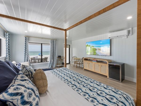 A modern bedroom with ocean view features a patterned bed, large TV, air conditioner, and a balcony with seating for relaxation.