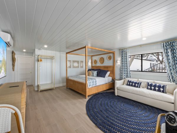 A modern bedroom with a canopy bed, sofa, blue rug, and TV, decorated in a nautical theme.