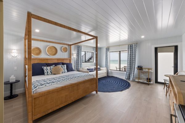 A spacious beachfront bedroom with a four-poster bed, nautical decor, and large windows overlooking the ocean.