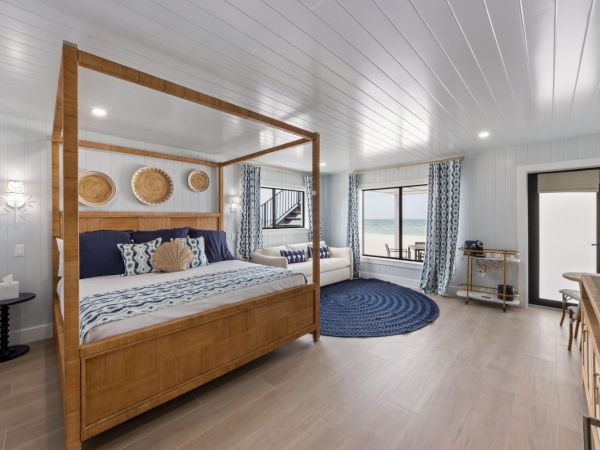 A spacious beachfront bedroom with a four-poster bed, nautical decor, and large windows overlooking the ocean.