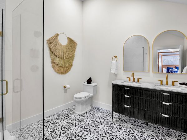 A modern bathroom features a glass shower, decorative wall accents, double vanity with mirrors, and patterned floor tiles.