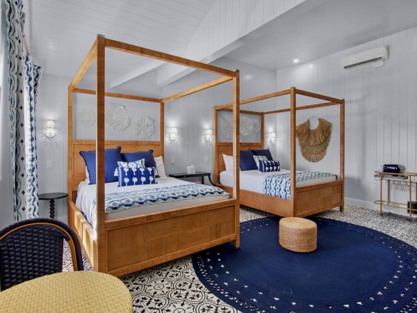 A stylish bedroom with two wooden canopy beds, blue accents, patterned floor, round rug, wicker stool, and wall decor.