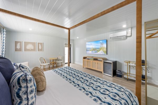 The image shows a stylish bedroom with a four-poster bed, patterned bedding, a wall-mounted TV, and a seating area.