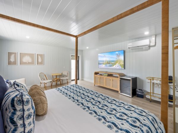 The image shows a stylish bedroom with a four-poster bed, patterned bedding, a wall-mounted TV, and a seating area.