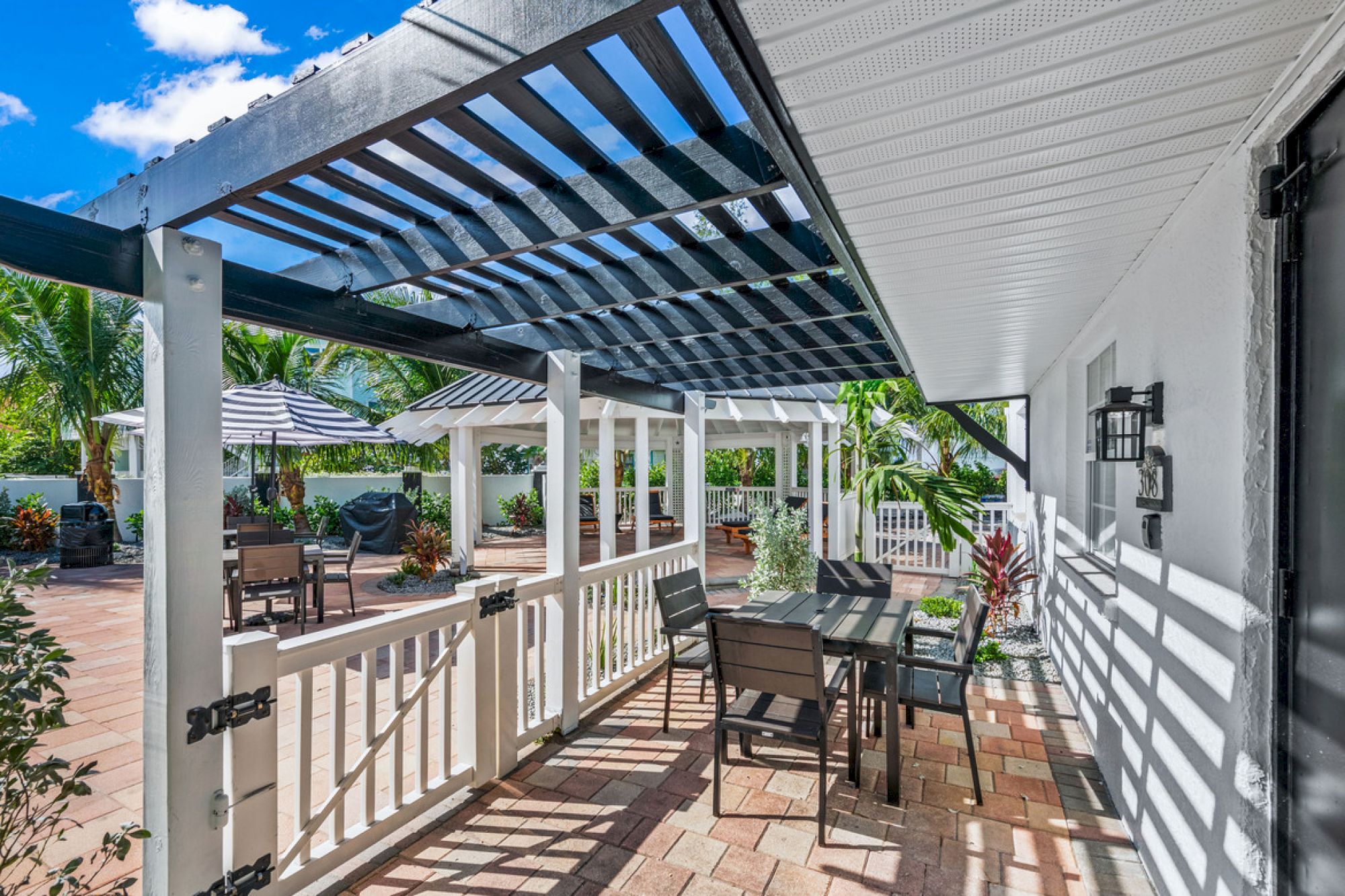 A sunny patio with a table and chairs under a pergola, surrounded by plants and outdoor seating, exudes a relaxing atmosphere.