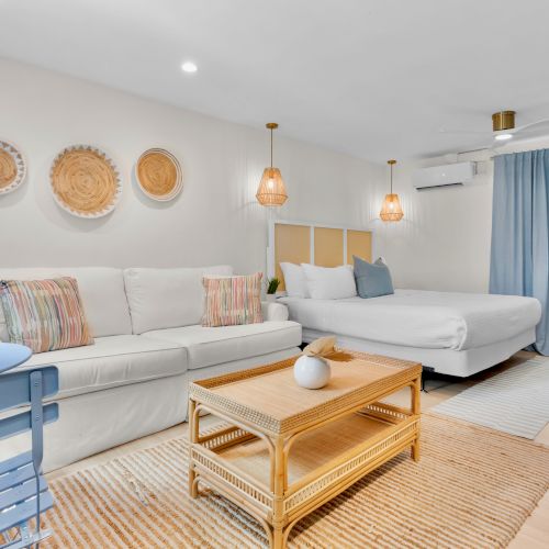 Bright modern lounge with a white sectional, woven coffee table, blue curtains, pendant lights, and rattan wall d&eacute;cor.