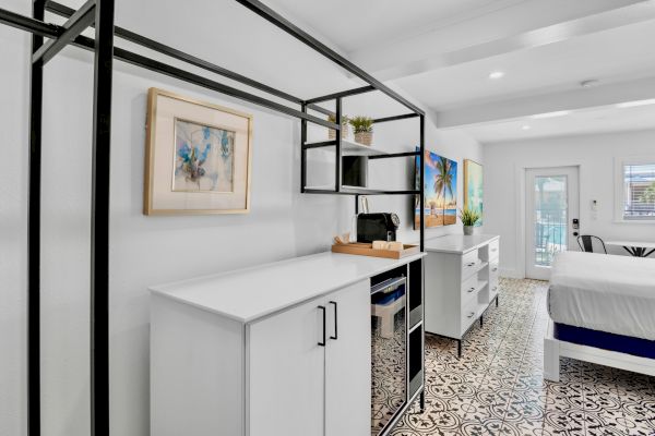 A modern, white room with patterned flooring features a bed, cabinetry, artwork, and a wall-mounted TV.
