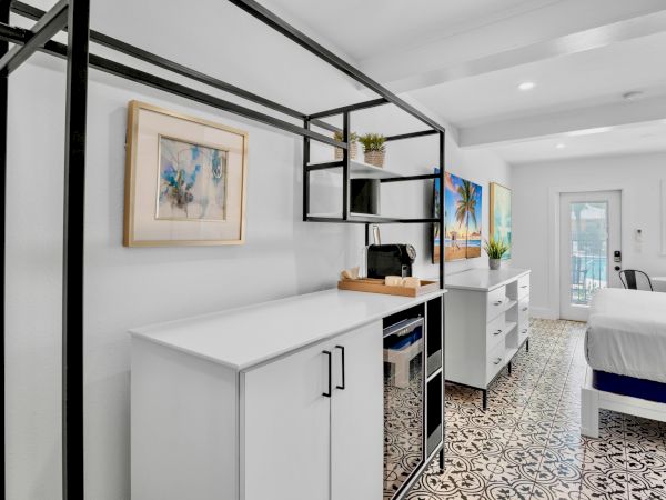 A modern, white room with patterned flooring features a bed, cabinetry, artwork, and a wall-mounted TV.