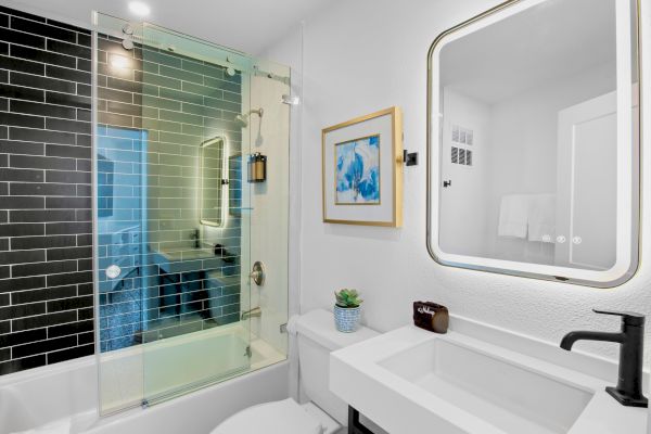 A modern bathroom with a glass shower, black tiles, framed art, a sink, and a mirror. It has a minimalistic and clean design.