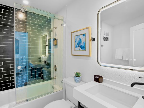 A modern bathroom with a glass shower, black tiles, framed art, a sink, and a mirror. It has a minimalistic and clean design.