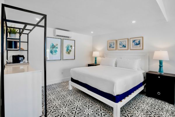 A modern bedroom with a large bed, patterned floor, art on the wall, nightstands, lamps, and a shelving unit.