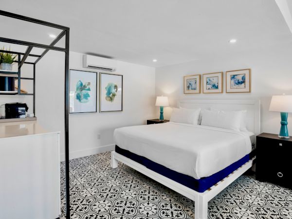 A modern bedroom with a large bed, patterned floor, art on the wall, nightstands, lamps, and a shelving unit.