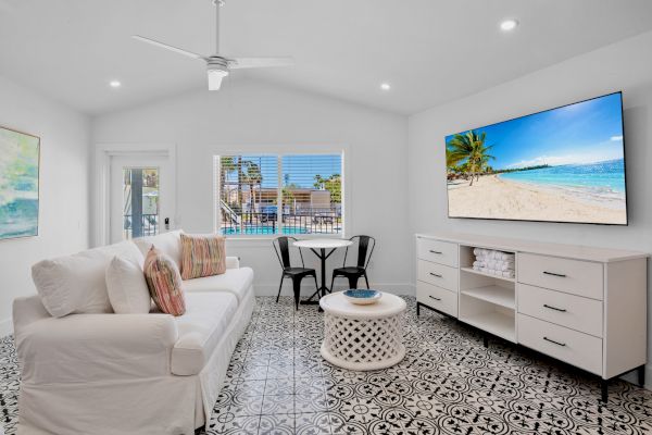 A bright living room with a white sofa, patterned floor, wall TV, small table and chairs, featuring beach decor.