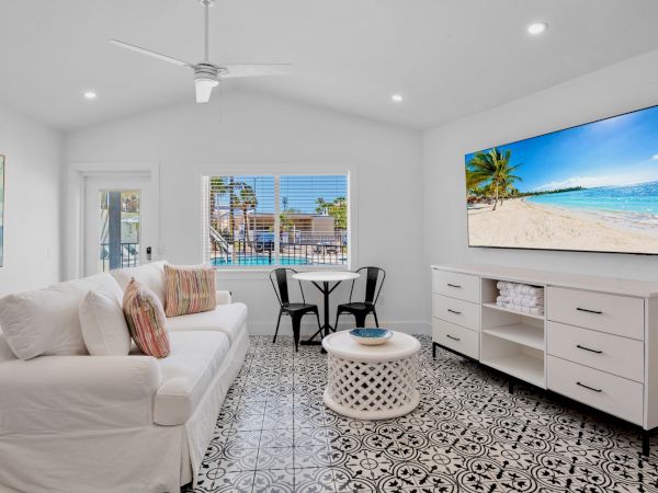A bright living room with a white sofa, patterned floor, wall TV, small table and chairs, featuring beach decor.