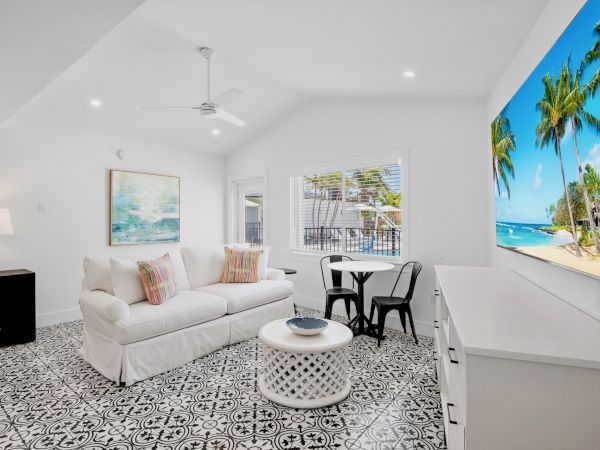 A bright living room features a white couch, stylish patterned floor, and a large wall-mounted TV displaying a beach scene.