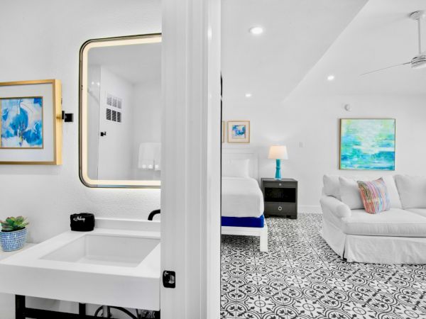 The image shows a modern, bright room with a patterned floor, a sofa, bed, and a bathroom with a sink and mirror.
