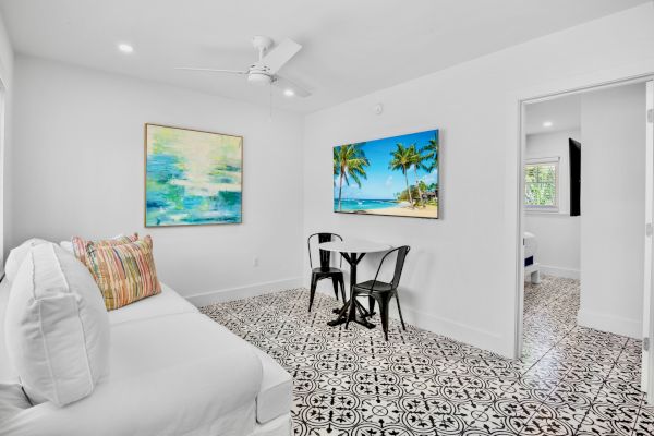 A bright room with patterned floor tiles, a white couch, colorful cushions, two paintings, and a small table with two chairs.