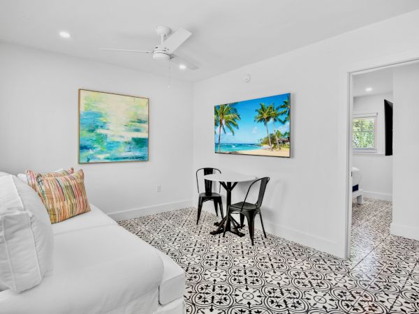 A bright room with patterned floor tiles, a white couch, colorful cushions, two paintings, and a small table with two chairs.