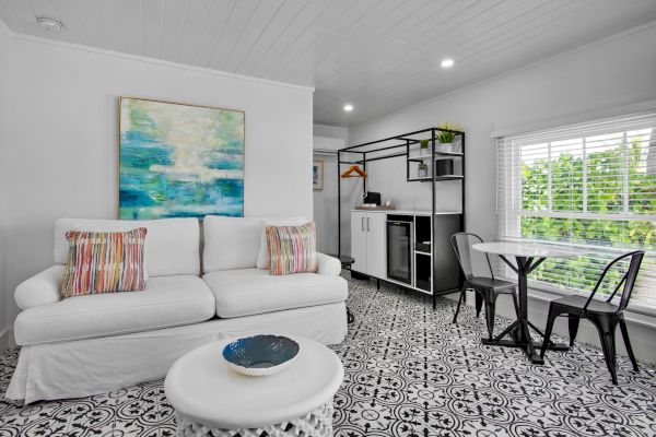 A modern living room with a white sofa, colorful pillows, abstract painting, round table, and chairs, featuring black and white patterned floor.