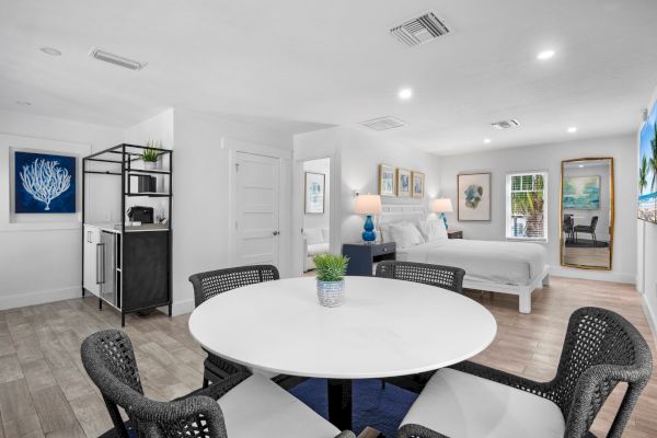 Modern open-plan bedroom with kitchenette, dining table, and artwork; bright and airy with neutral tones.
