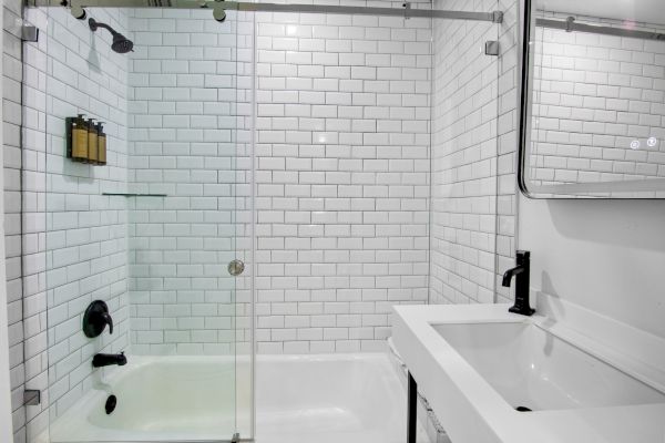 A modern bathroom with white subway tiles, a bathtub with a glass door, and a sink with a mirror above it.