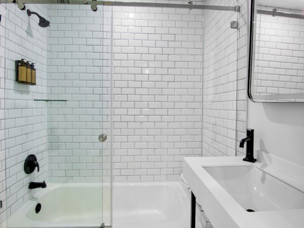 A modern bathroom with white subway tiles, a bathtub with a glass door, and a sink with a mirror above it.