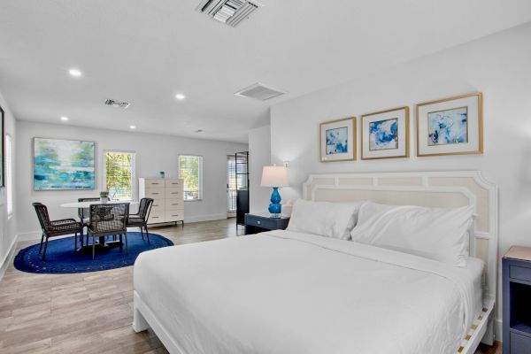 A modern bedroom with a white bed, abstract art, a small dining area, and a blue rug under a round table with chairs.