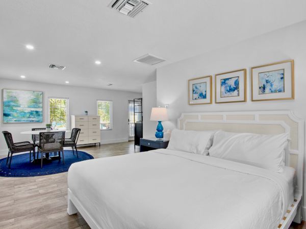 A modern bedroom with a white bed, abstract art, a small dining area, and a blue rug under a round table with chairs.