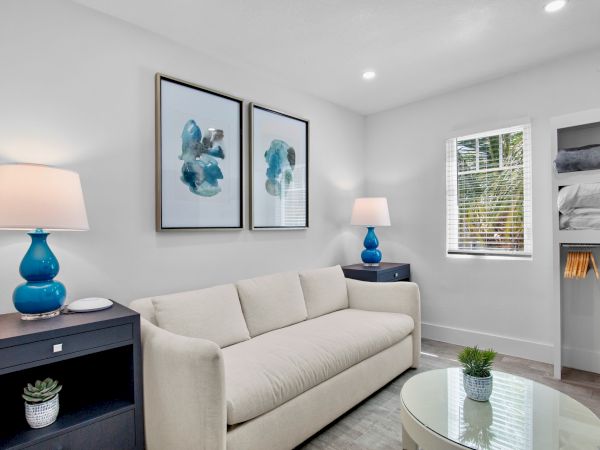 A modern living room with a beige sofa, blue lamps, abstract wall art, and minimal decor in a bright space.