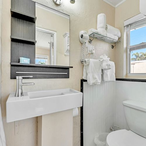A compact bathroom features a sink, mirror, shelves, towels, and a window, creating a tidy and functional space.
