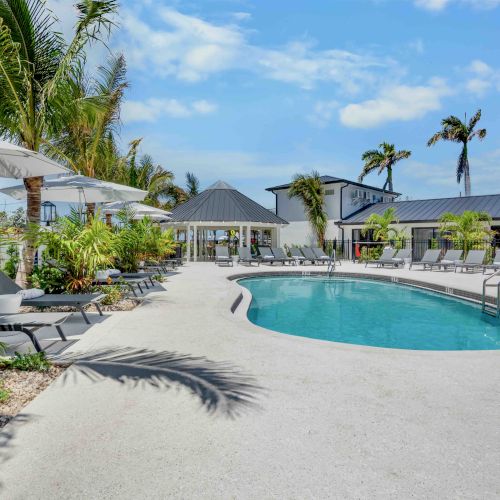A sunny tropical resort with a winding pool, palm trees, blue skies, and thatched-roof huts&mdash;perfect for lounging and beach vibes.