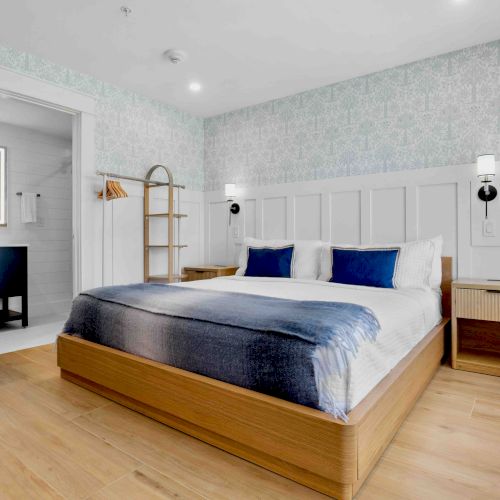 A modern bedroom with a wooden floor, a low-profile bed, a lime chair, a desk, built-in wardrobe, and soft natural light from a large window.