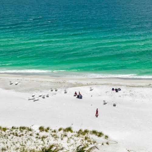 A scenic beach with white sand, clear turquoise water, and a few people lounging under umbrellas and tents scattered along the shore.
