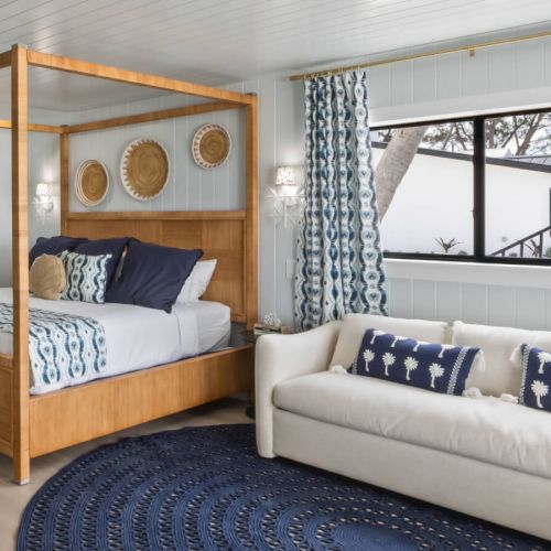 A bedroom features a canopy bed, couch, blue accents, patterned curtains, wall decor, and a large window with a view.