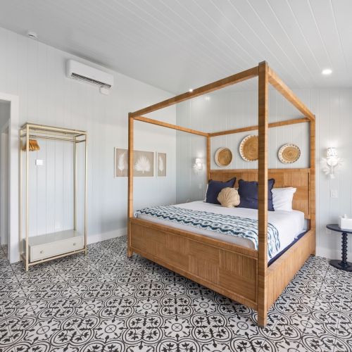 A stylish bedroom features a four-poster bed, patterned floor tiles, and light decor, creating a cozy and inviting atmosphere.