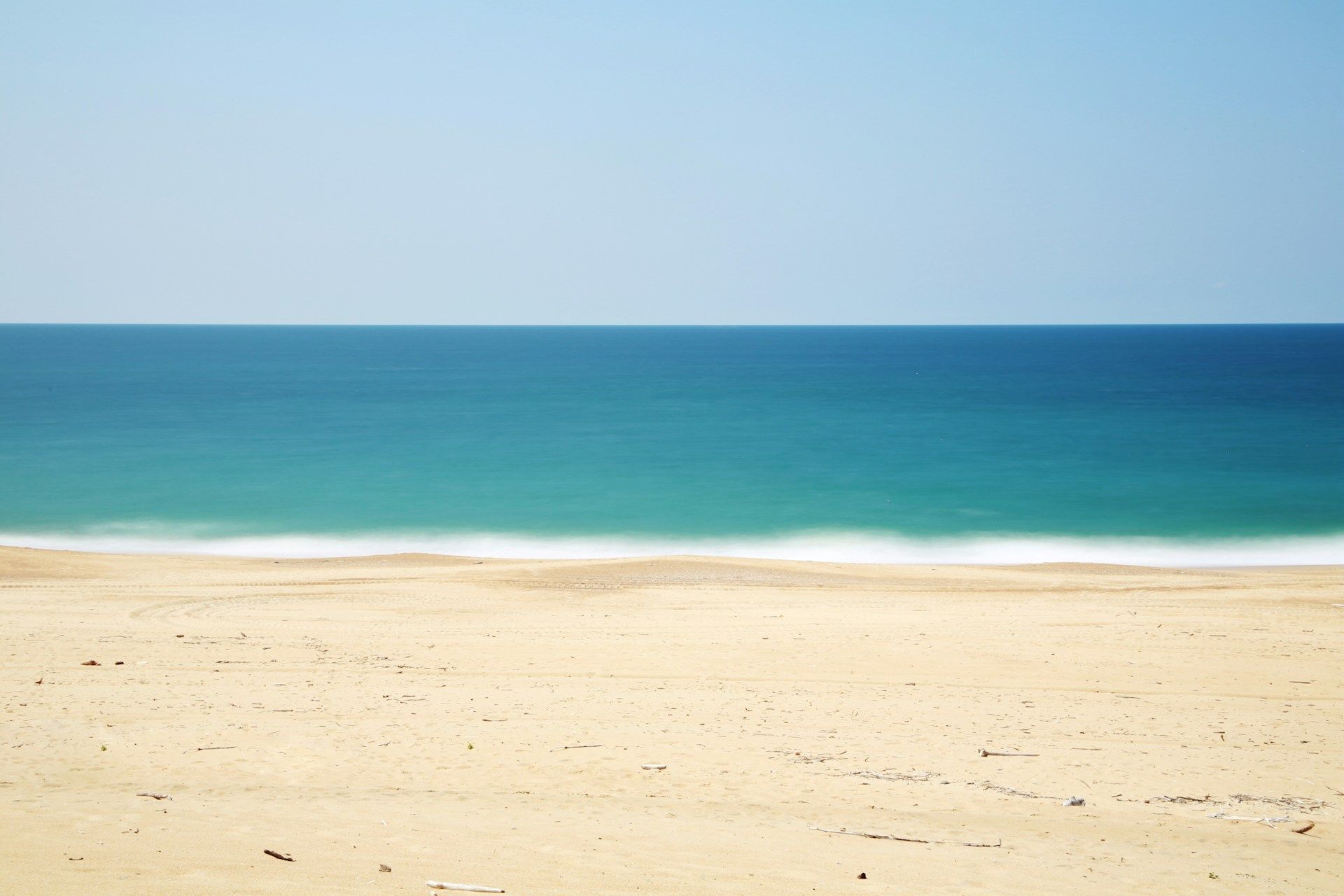 A tranquil beach scene with pale sand and calm turquoise-blue ocean under a clear blue sky, creating a serene and peaceful atmosphere.