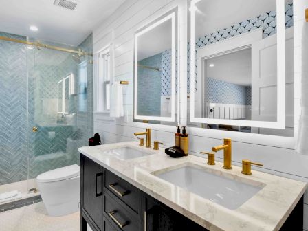A modern bathroom with double vanity, marble countertop, gold fixtures, and a glass shower. 140 characters. End the sentence.