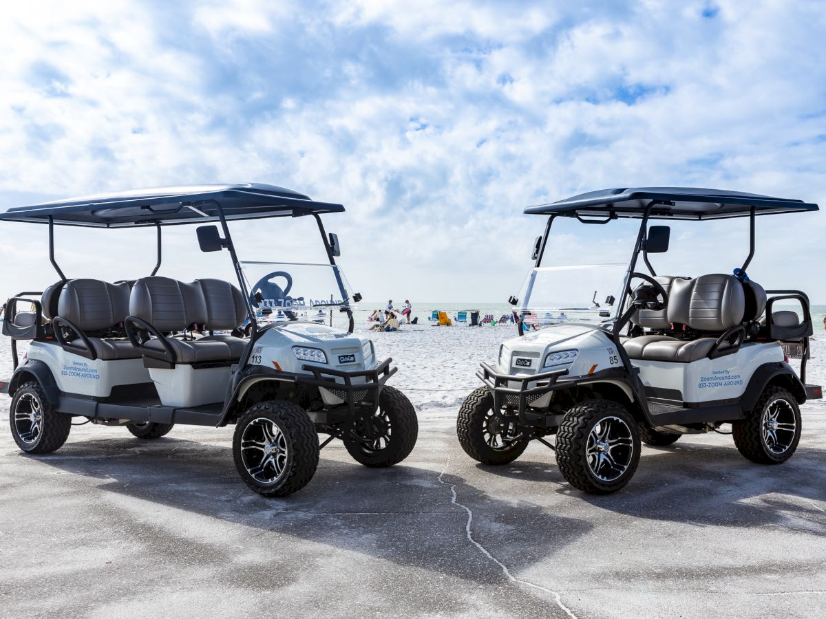 Two shiny golf carts parked on a sunny beach, ready for a ride under blue skies.