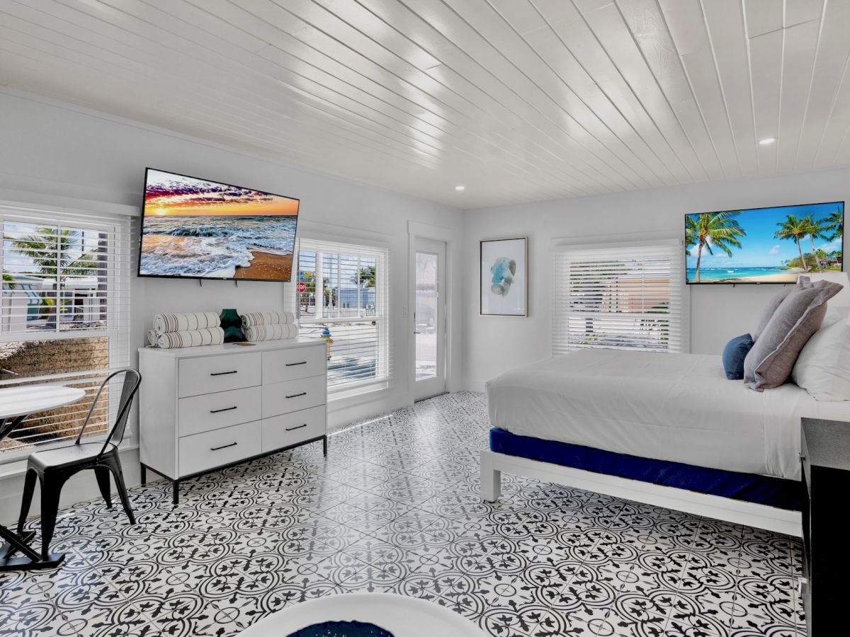 Bright seaside-themed living room with patterned tile floor, white sofas, dresser, and two wall-mounted TVs.