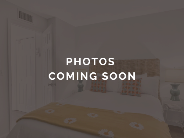A bright bedroom with a neatly made bed and pillows, with the text &ldquo;PHOTOS COMING SOON&rdquo; overlaid on the image.