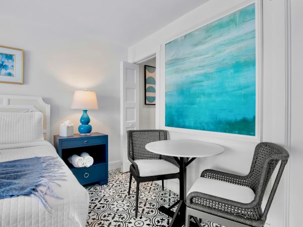 Bright bedroom lounge area with a blue lamp, patterned floor tiles, chairs, and a large turquoise abstract wall art.