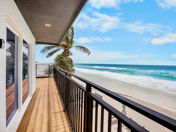 A seaside balcony with palm tree by the rail, facing waves and a bright blue sky.