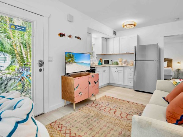 Bright kitchen and living area with white cabinets, TV, fridge, stove, and a cozy sofa by large patio doors.