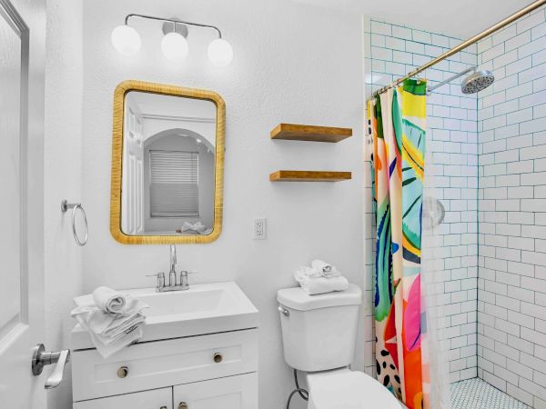 A bright modern bathroom with a white vanity, framed mirror, shower with colorful curtain, and blue-tiled walls, ready for a spa day.