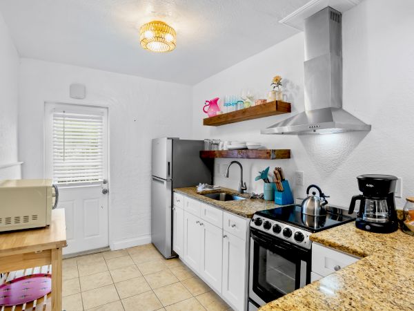 Bright white kitchen with an island, stove and hood, sink, shelves, fridge, and small appliances on the counters.