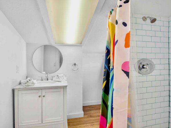 Bright bathroom with a sink vanity and round mirror, plus a tiled shower with a colorful character-pattern curtain and showerhead.