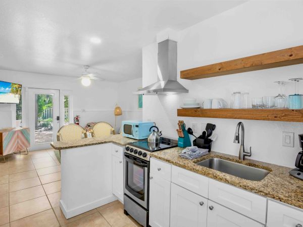 Bright modern kitchen with granite counters, stove and hood, plus glassware, utensils, and small appliances on the counters.