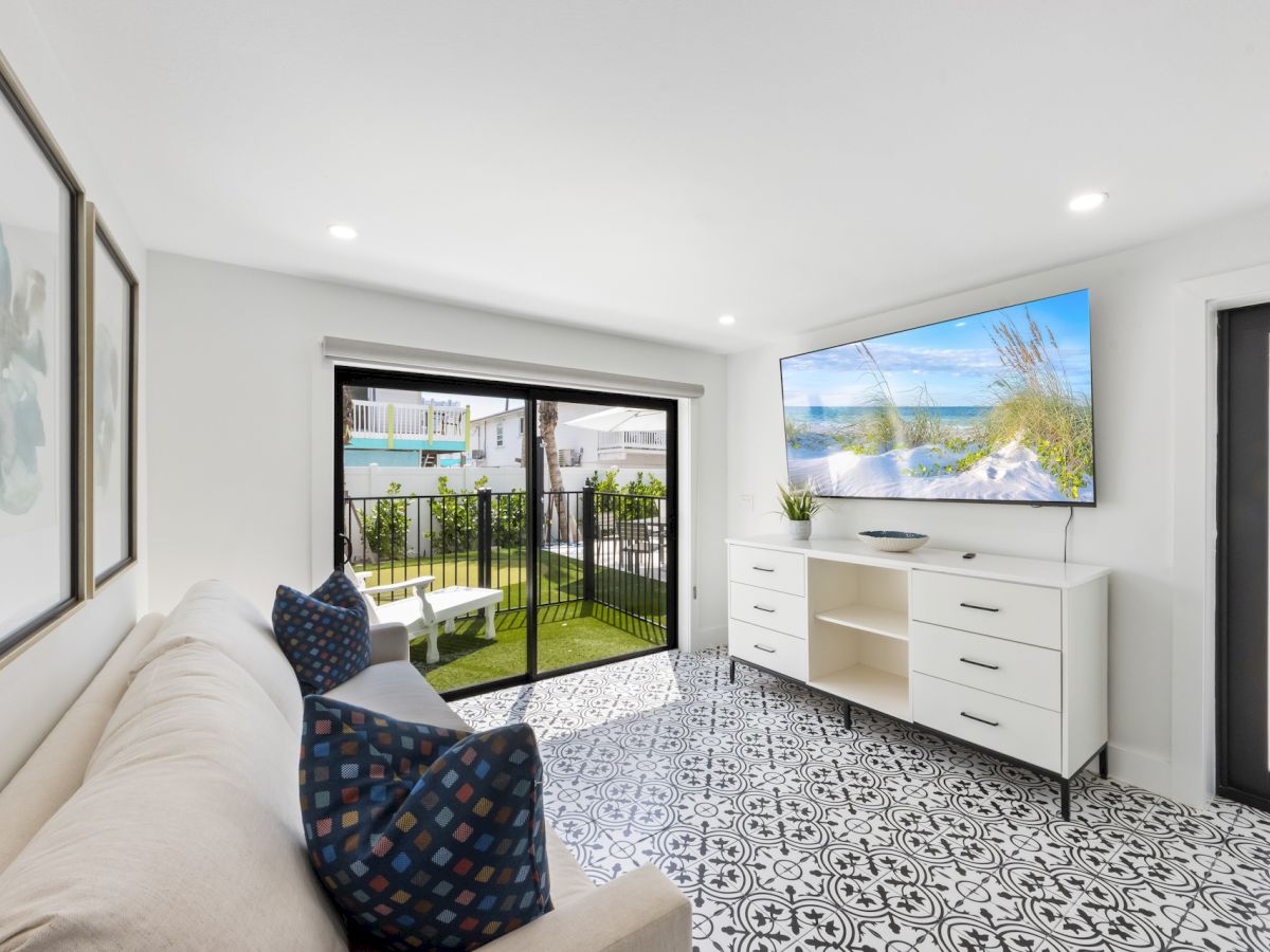 A bright modern living room with a couch, patterned tile floor, and sliding doors to a grassy patio with outdoor seating.