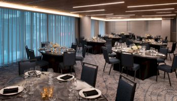 The image shows an elegant dining room setup with round tables, black chairs, and decorative table settings.